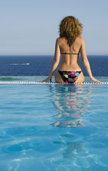 Girl sitting on edge of infiniti pool gazing out to sea - if you are taking your contract hire or lease car abroad this year make sure you have the correct documentation, which includes a VE103B for the company car