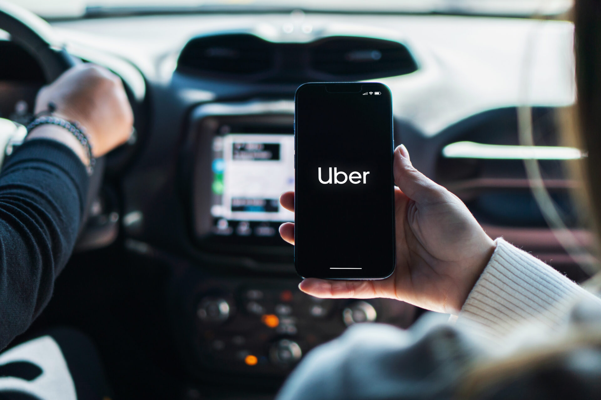 Girl inside car holding smartphone with Uber app on screen. Rio