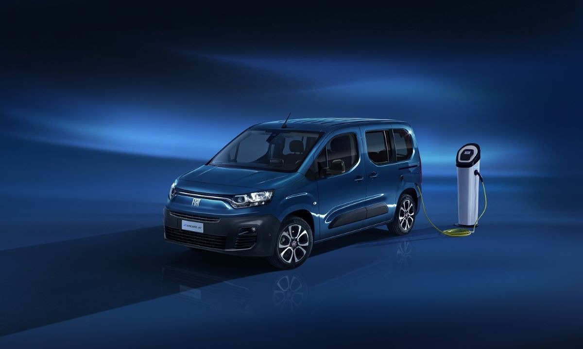 Blue Fiat Doblo electric van next to a white charging station on dark blue background.