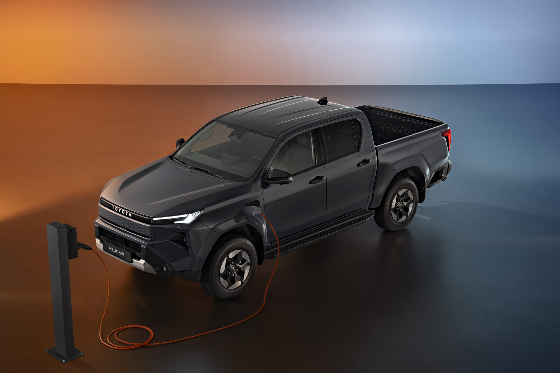 Black Toyota Hilux pickup truck connected to an EV charging station against orange and blue gradient background.