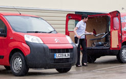 Two red vans parked side by side with drivers standing between them on an industrial estate.
