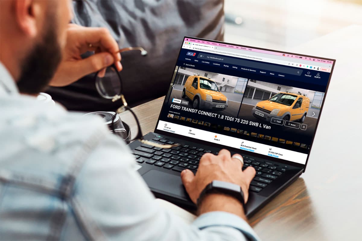 Man viewing Ford Transit Connect van listings on laptop screen.