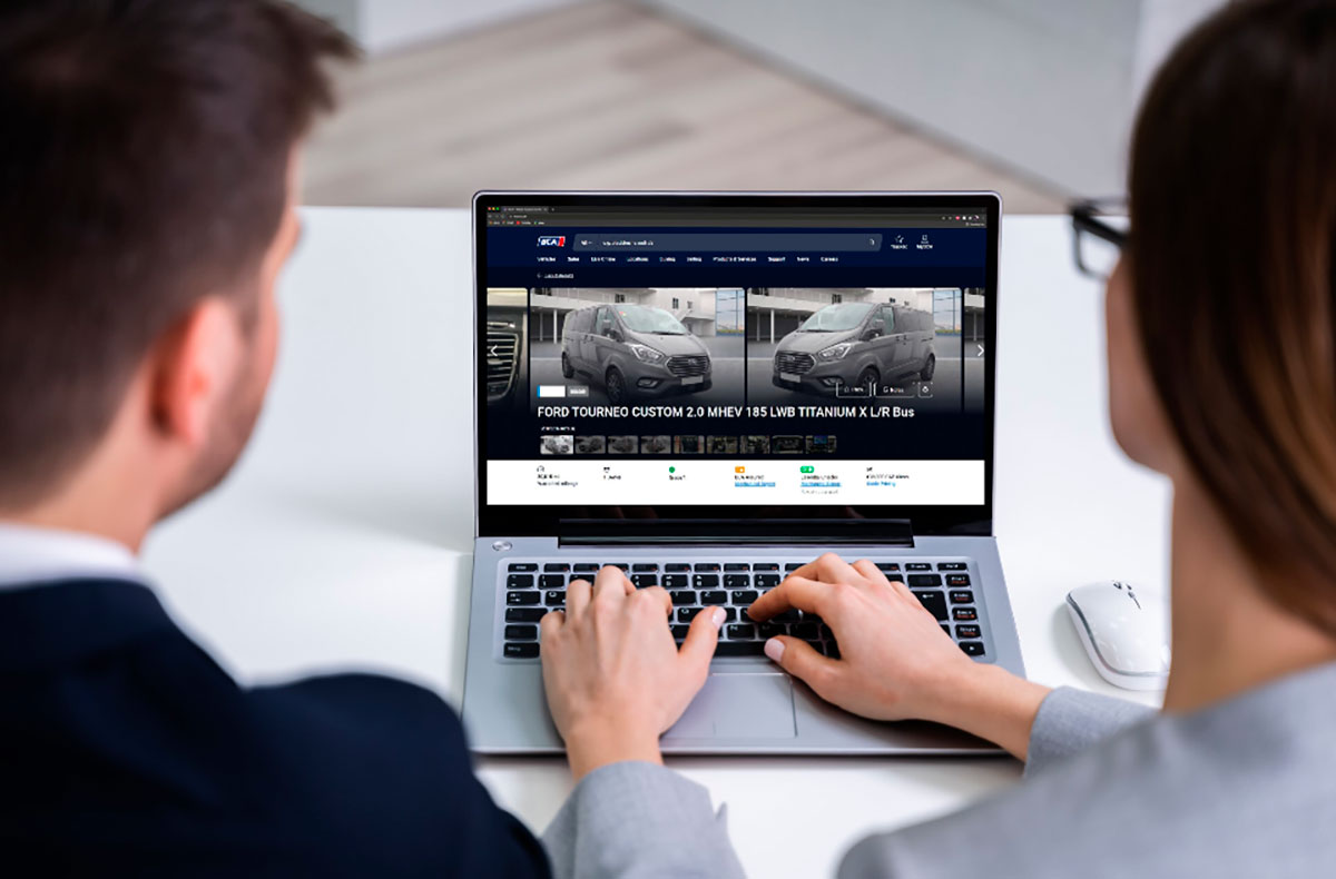 Two people viewing used van listings on laptop screen, browsing vehicle inventory website.
