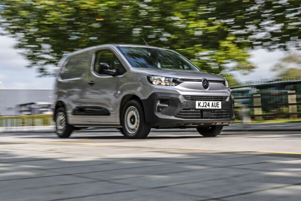 Silver Citroën Berlingo van driving on road with blurred green trees and buildings in background.