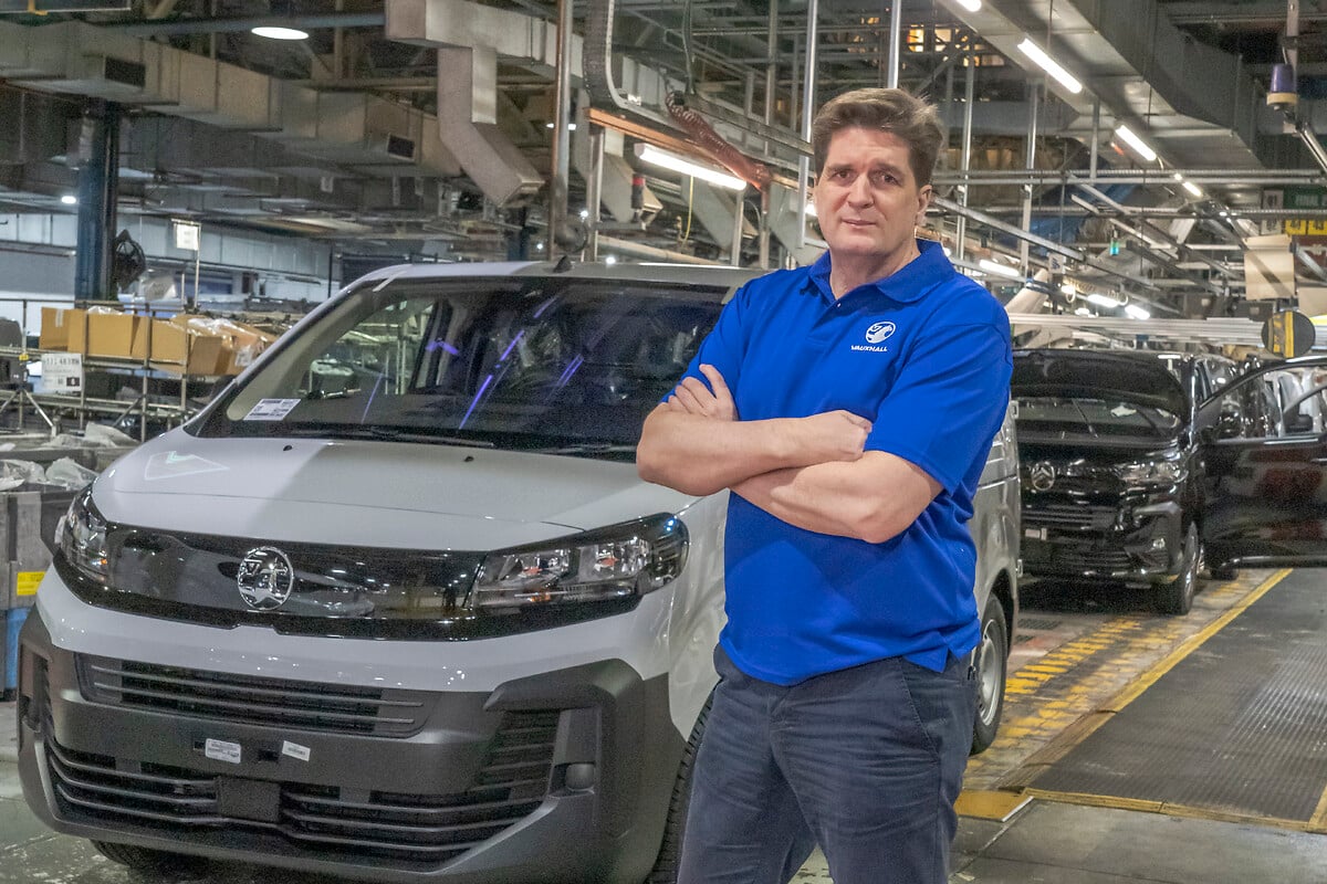 Factory worker in blue shirt standing beside white Toyota vehicle on manufacturing production line.
