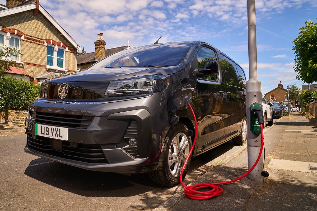 Black Vauxhall electric van charging at public charger on residential street, red cable connected to vehicle.