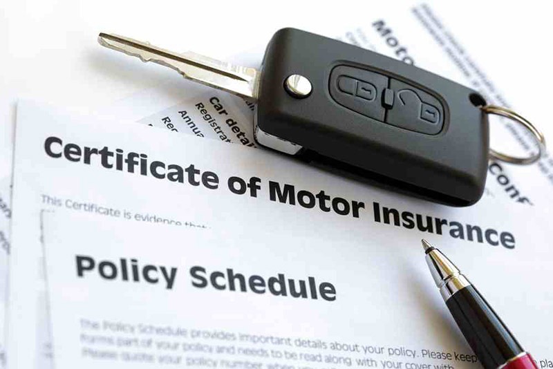 Car key resting on Certificate of Motor Insurance and Policy Schedule documents.