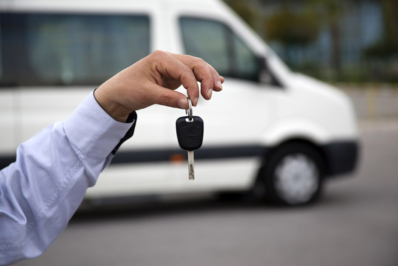 Hand holding van key with white commercial vehicle in background