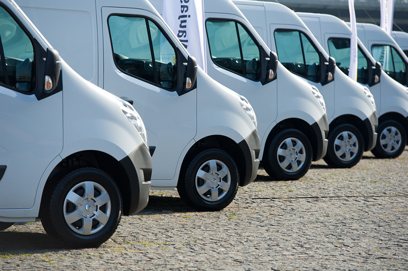 Row of white commercial vans parked in line on gravel surface.