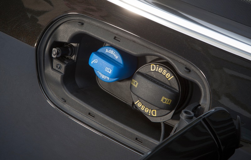 Open fuel door on diesel van showing blue AdBlue cap and diesel filler cap with charging cable attached.