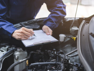 Auto check, car service shop concept. Automobile repairman writing job checklist on clipboard, mechanic checking engine to estimate repair machine, inspecting maintenance by engineer at vehicle garage