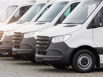 Fleet new modern electric hybrid hydrogen or diesel white vans parked in line row outdoors. Cargo freight industrial courier transportation logistics service. Commercial vehicle maintenance insurance