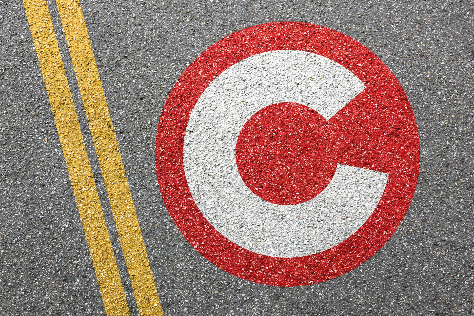 Copyright symbol painted red and white on road surface next to yellow centre line markings.