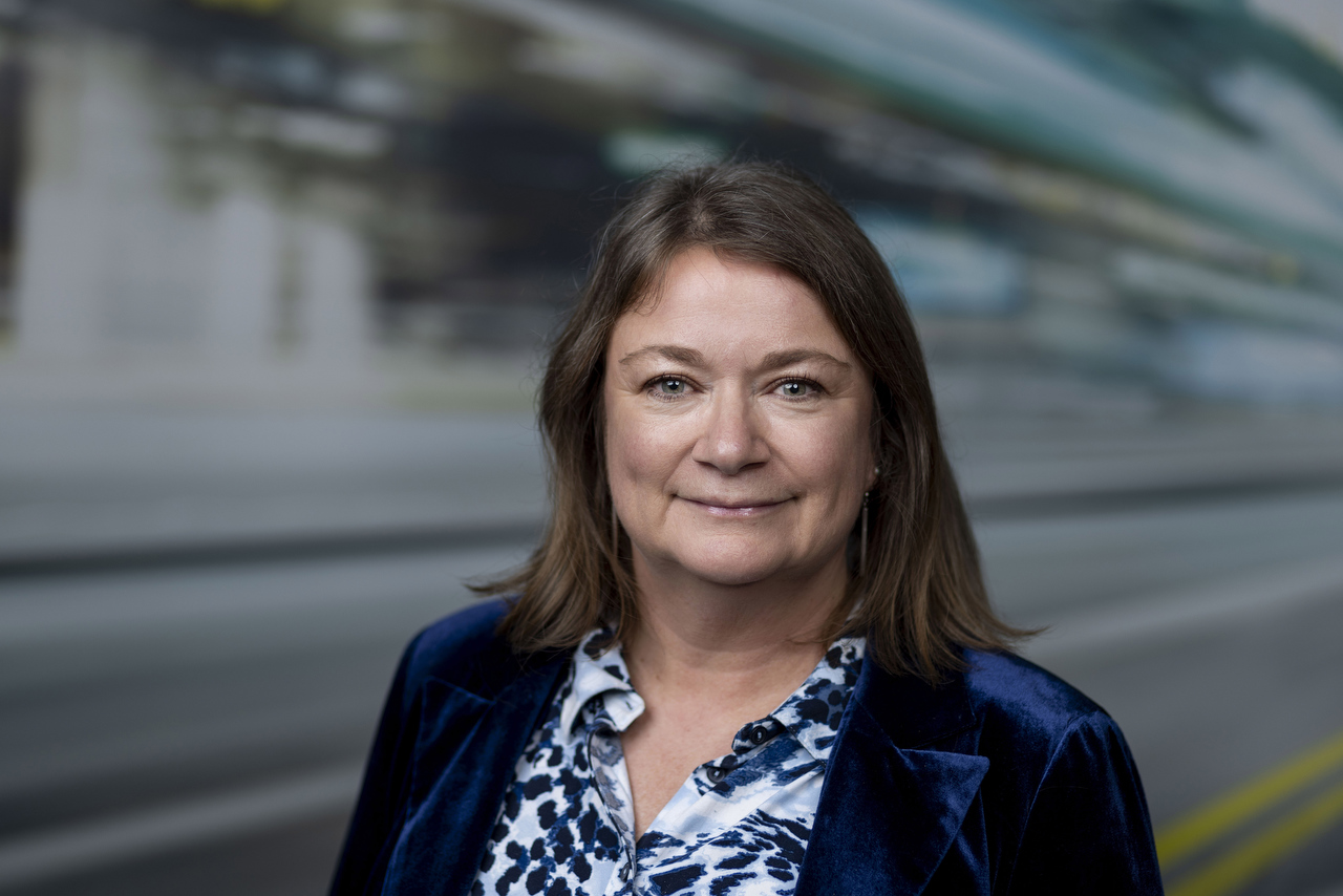 Woman in navy velvet jacket and patterned blouse standing in front of parked train.