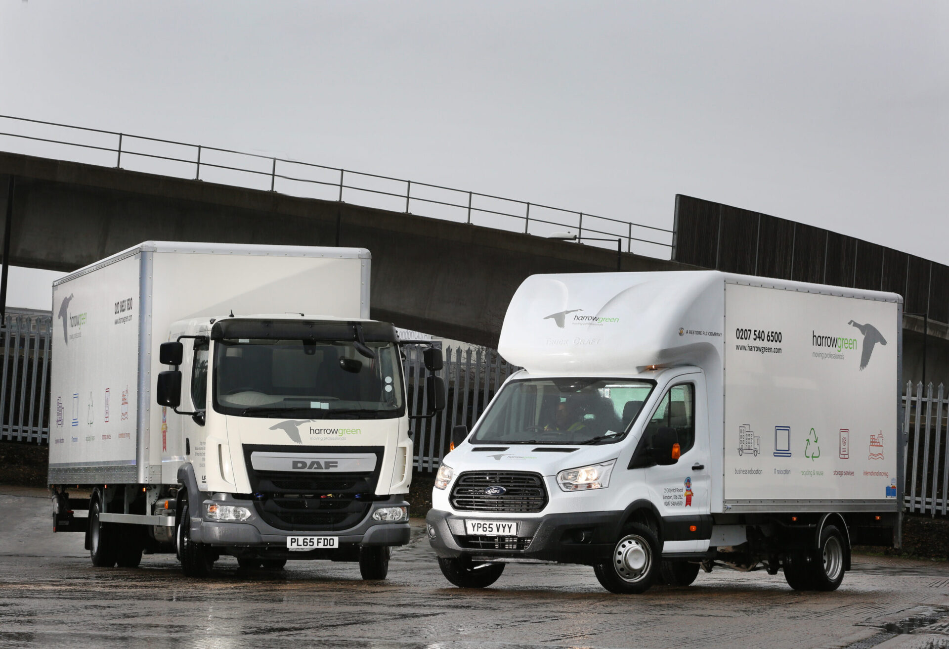 Two white commercial vehicles parked side by side on wet tarmac beneath a bridge, demonstrating Asset Alliance's contract…