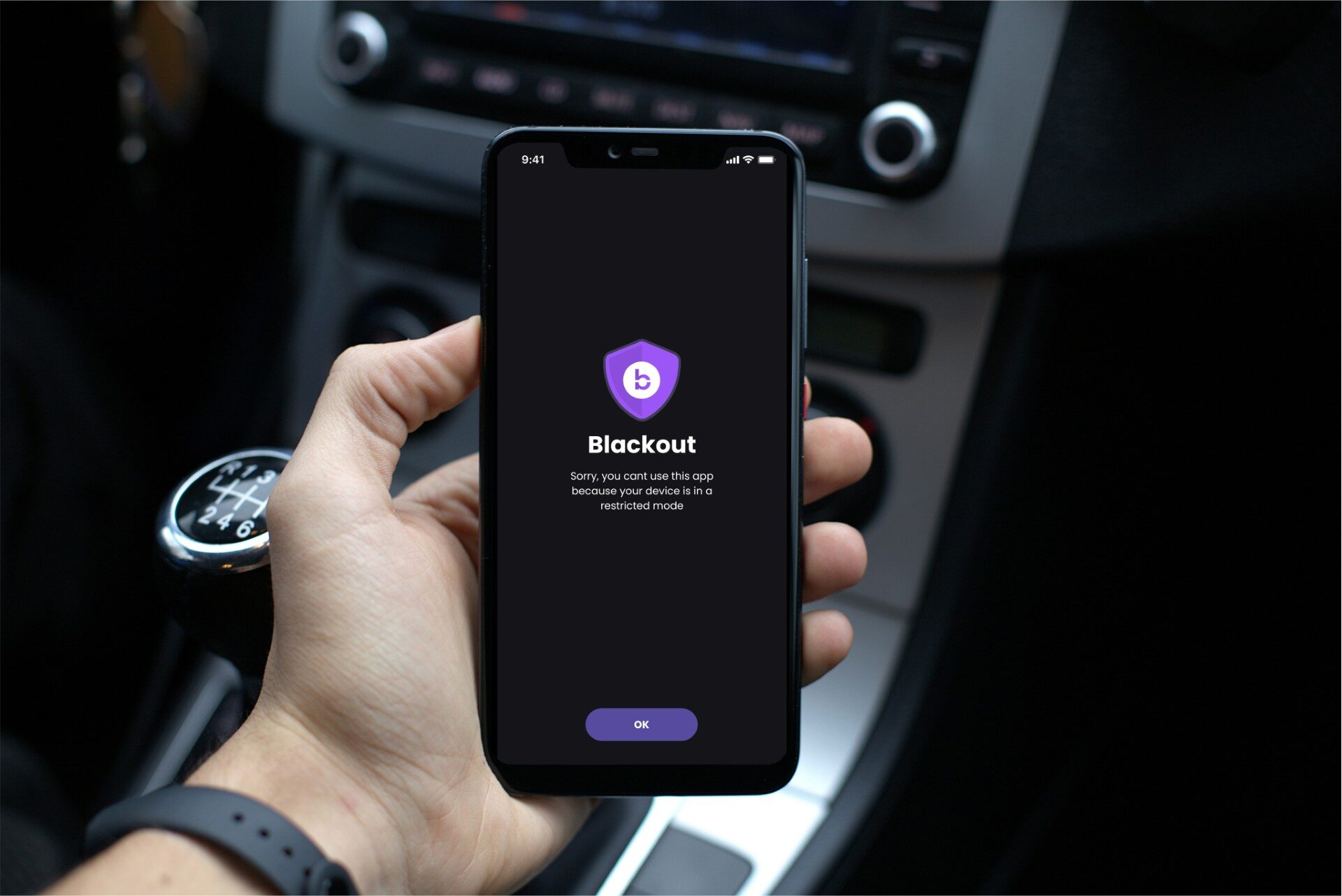 Hand holding smartphone displaying Blackout app screen with purple shield icon in car interior.