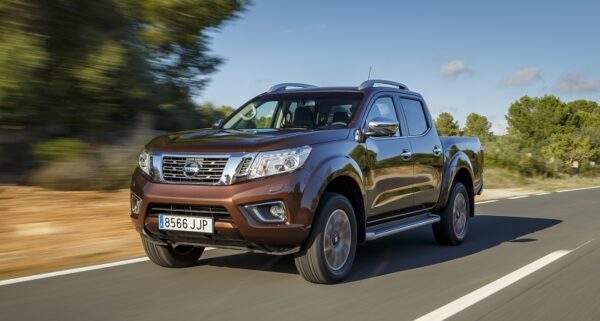 Nissan Navara NP300 double cab pick-up truck in bronze metallic driving on a rural road with green trees and clear sky.