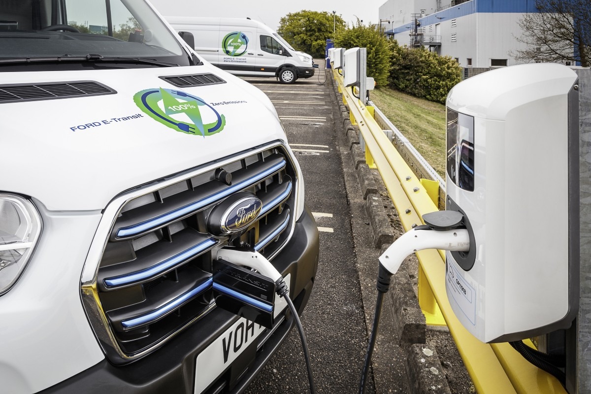 Ford E-Transit van charging at rapid charging station, with second van in background at depot.