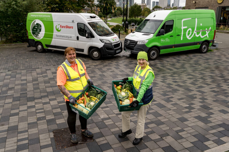 Two workers in high-visibility jackets hold crates of fresh produce in front of green Fentura and Felix branded delivery…