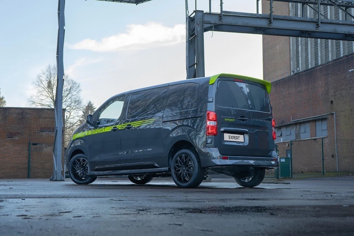 Peugeot Expert Sport van in black and lime green, parked in industrial courtyard showing rear three-quarter view.