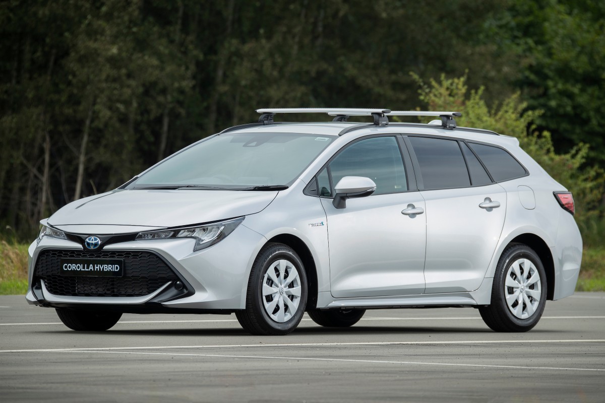 Silver Toyota Corolla Hybrid estate car with roof bars parked against woodland backdrop.