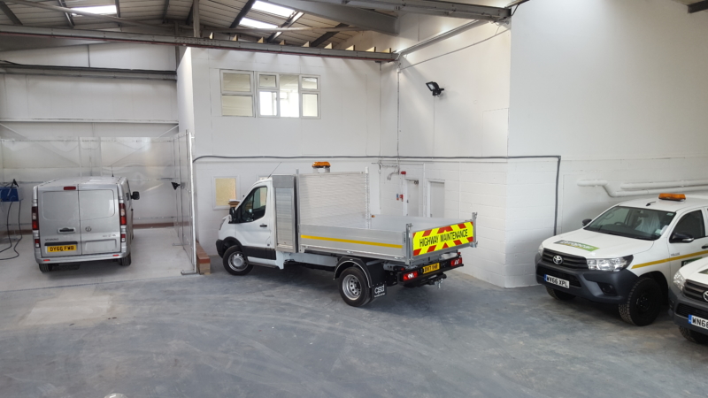 Europcar van hub warehouse interior with white delivery vans and emergency vehicles parked inside industrial facility.