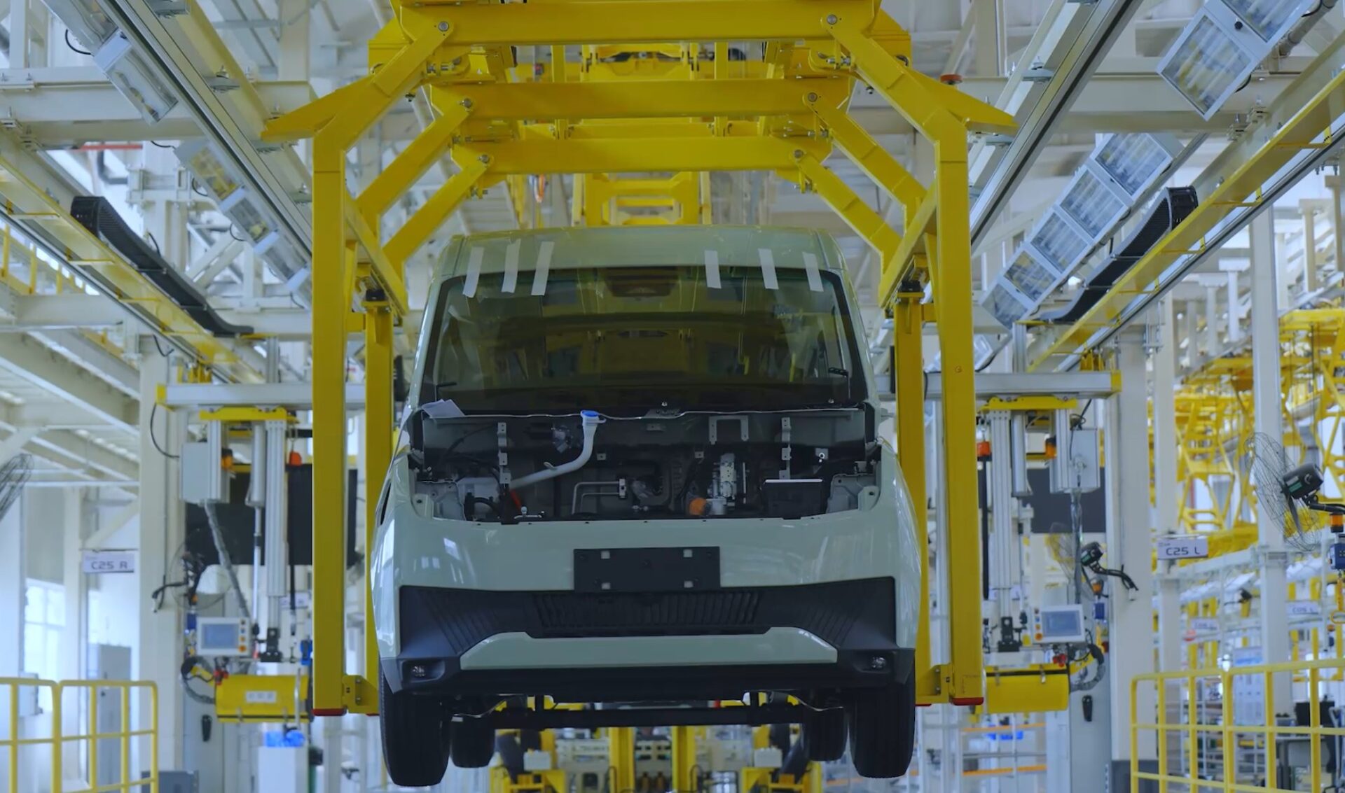 White and black electric van on yellow robotic assembly line in manufacturing facility.