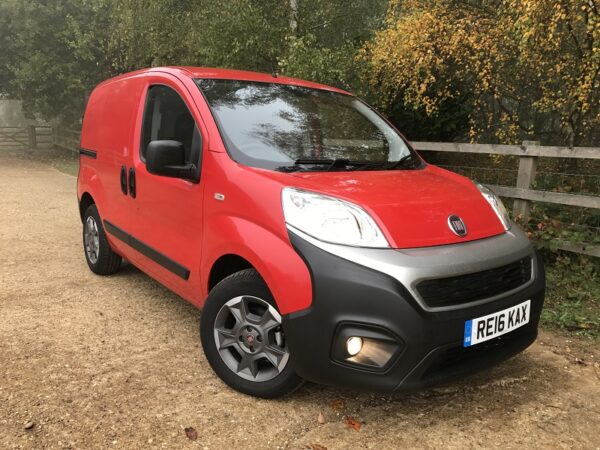 Red Fiat Fiorino compact van parked on gravel drive, front three-quarter view showing rounded design and single sliding door.