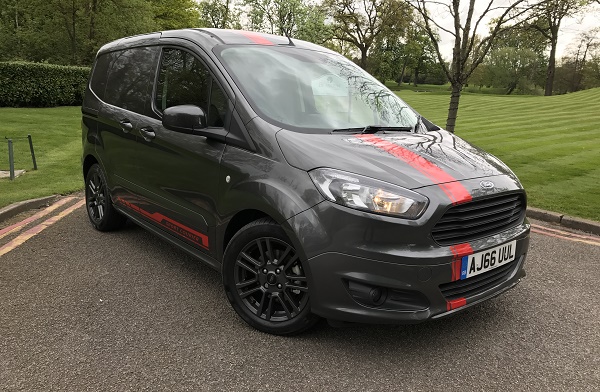 Dark grey Ford Transit Courier Sport with red accents parked on driveway with grass and trees behind.