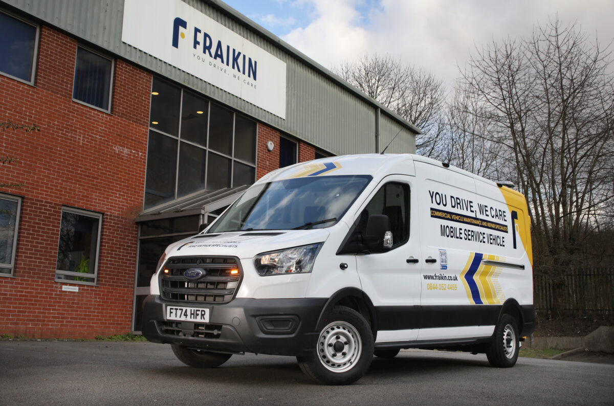 White Fraikin mobile service van parked outside brick warehouse building with bare trees in background.