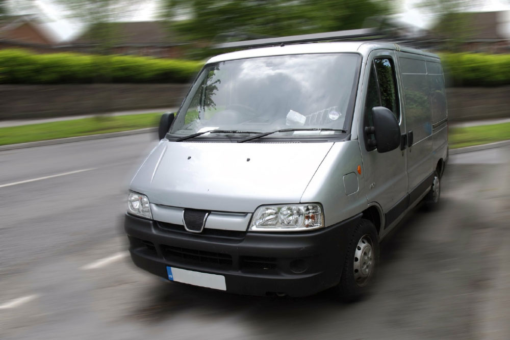 Silver and black panel van driving on suburban road with motion blur effect
