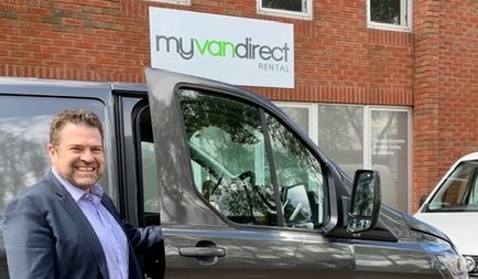 Man in blue shirt standing beside white van with Myvandirect branding and signage on brick building.