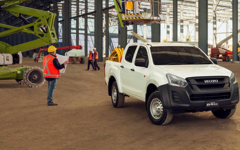 White Isuzu double cab pick-up truck on industrial site with worker in high-visibility clothing directing vehicle movement.