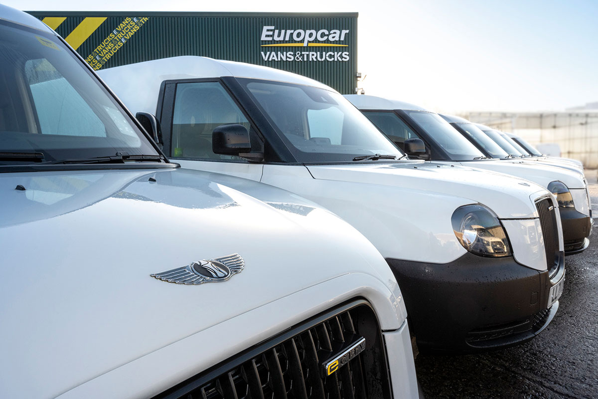 Row of white electric vans parked outside Europcar Vans & Trucks depot with open bonnet showing wing badge.