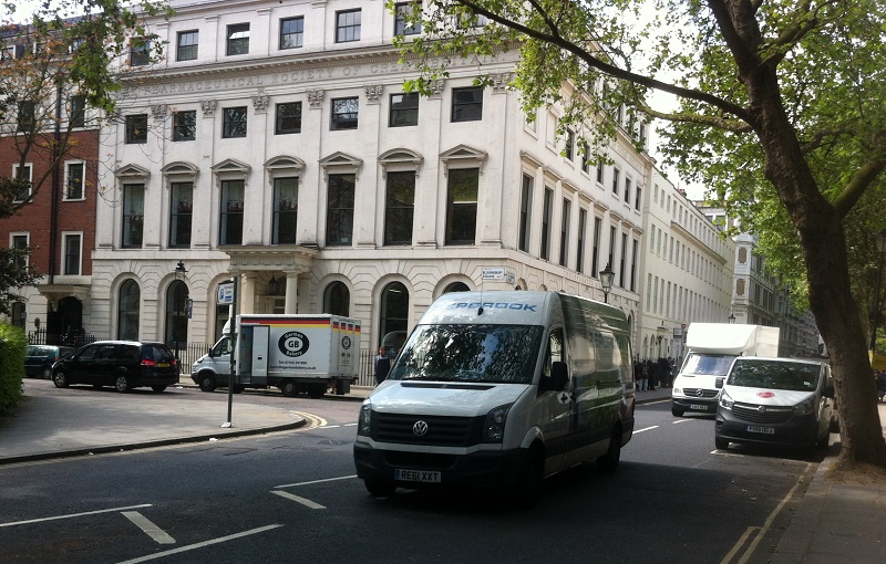 Parked vans on London street with grand Victorian buildings, including a low-emissions vehicle in foreground.