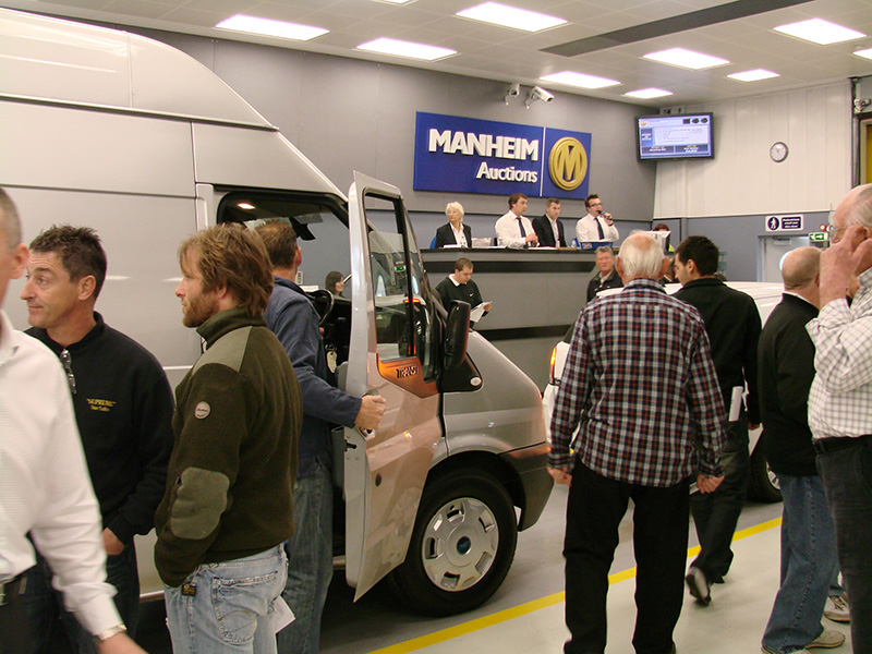 Manheim Auctions van sales floor with buyers and auctioneers examining a white commercial vehicle at the block.
