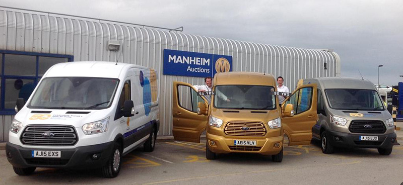 Three Ford Transit vans in white, gold and grey parked at Manheim Auctions with staff celebrating the Transit's 50th…