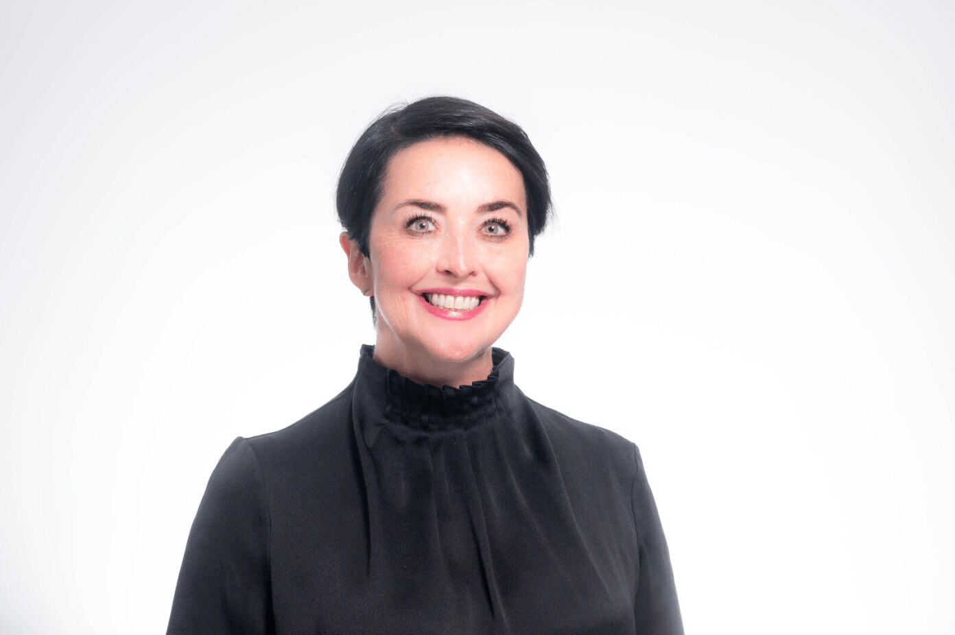Woman with short dark hair wearing black turtleneck against white background, smiling at camera.