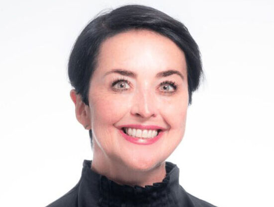 Woman with dark hair smiling at camera, wearing black turtleneck against white background.