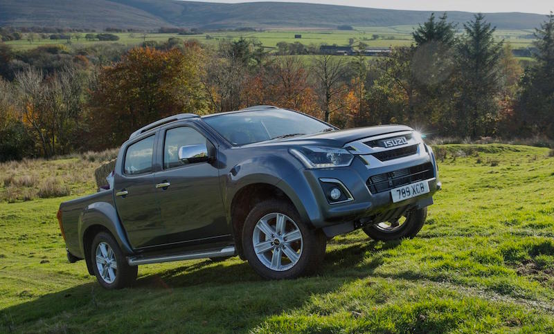 Isuzu D-MAX pickup truck parked on grass with rolling hills and autumn woodland in background.