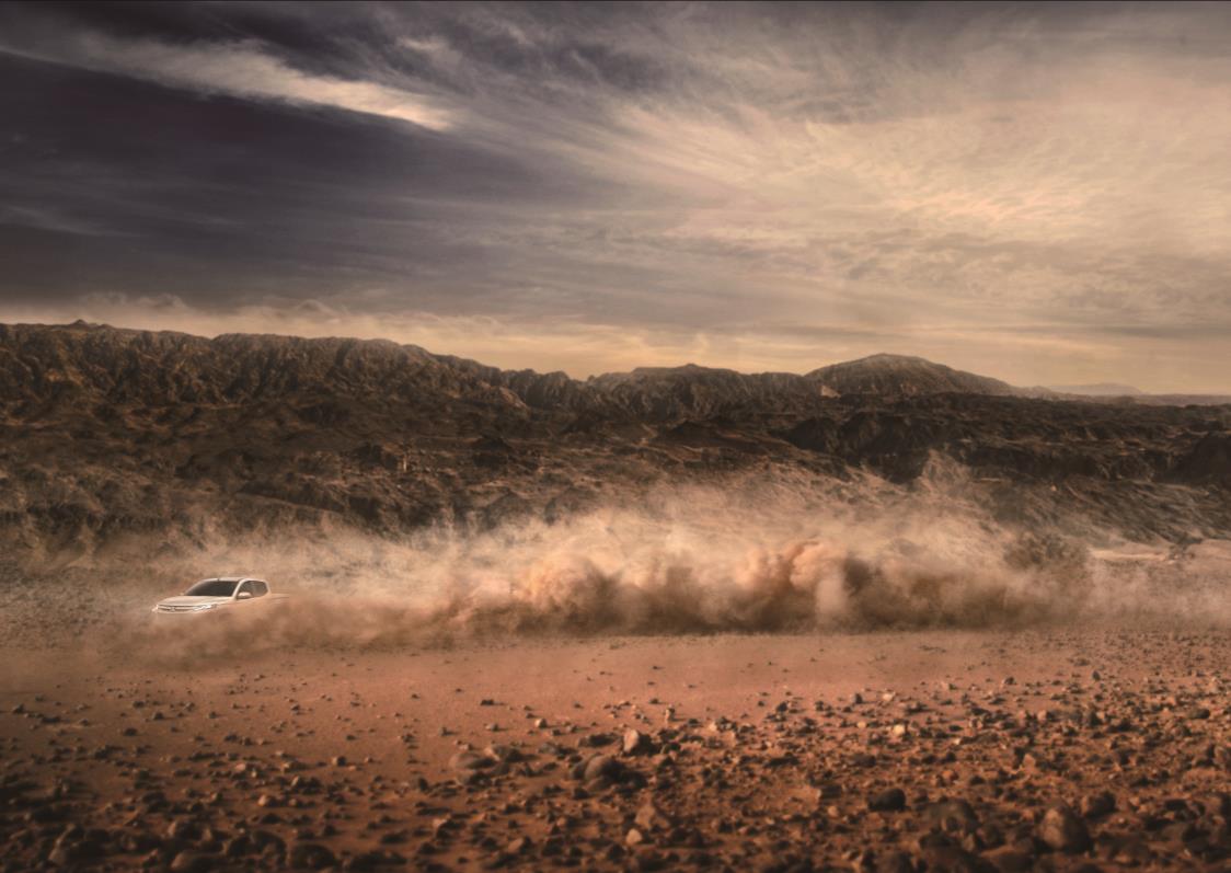 White Mitsubishi L200 kicking up dust cloud whilst driving across desert terrain with rocky mountains in background.