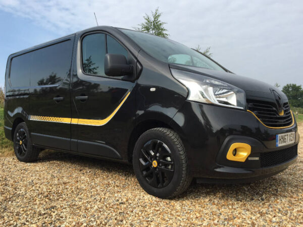 Black and yellow taxi van parked on gravel, demonstrating headlight design and visibility features.