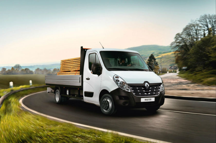 White Renault tipper van with wooden drop-side bed travelling on curved countryside road with hills in background.