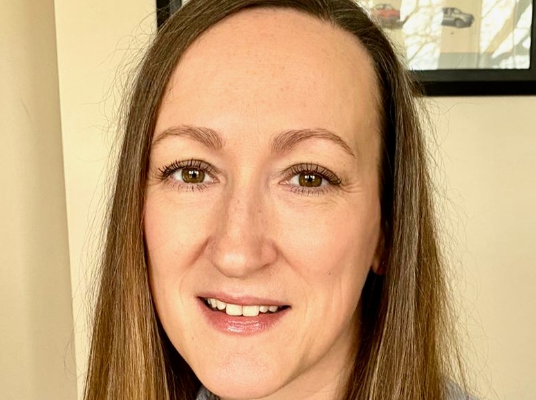 Woman with long brown hair smiling at camera in an office setting.
