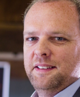 Man with beard and receding hairline smiling at camera, professional headshot.
