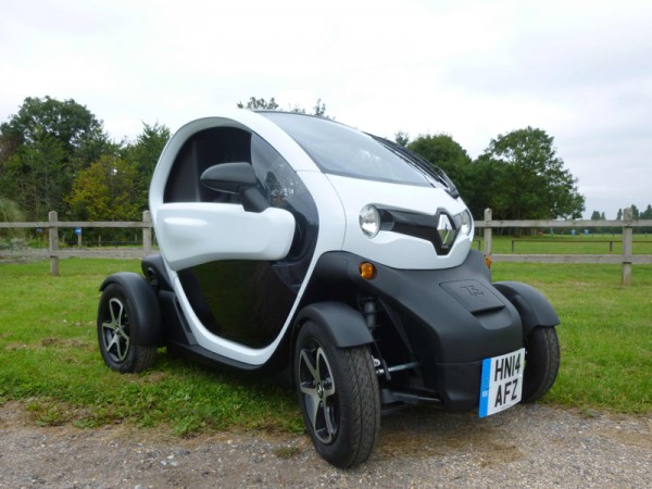 White and black Renault Twizy Cargo electric vehicle parked in countryside setting with green fields behind.
