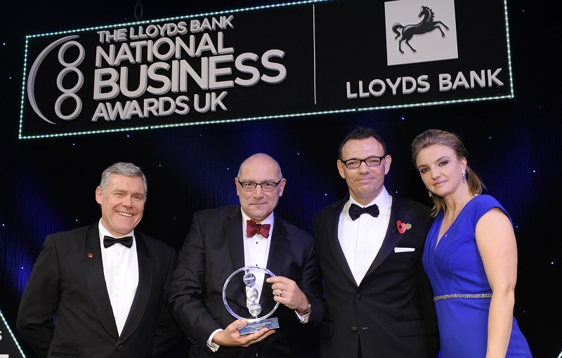 Four people in formal attire at Lloyds Bank National Business Awards UK ceremony, man second from left holding glass award.