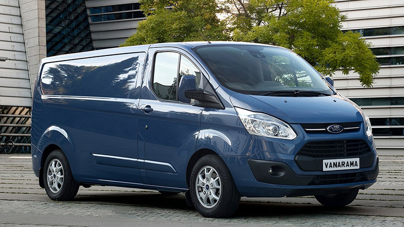 Blue Ford Transit Custom van parked in front of modern building with trees