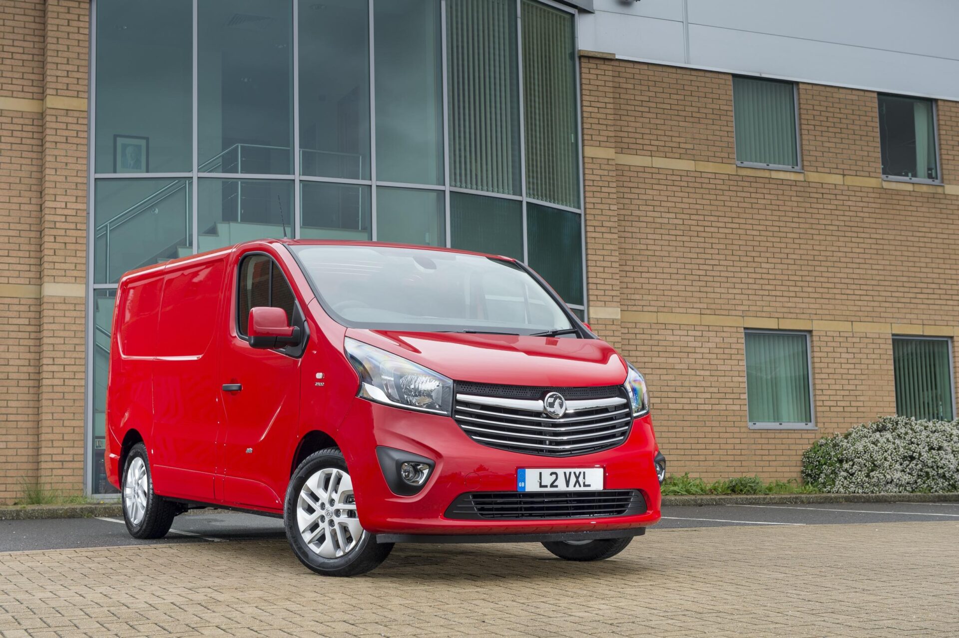 Red Vauxhall Vivaro van parked outside brick office building with large windows.