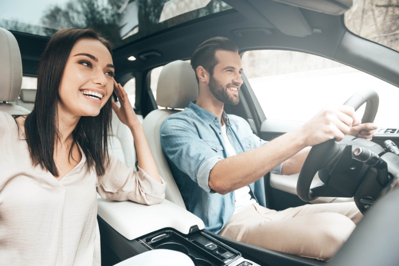 Young couple smiling inside convertible car with man driving and woman in passenger seat.